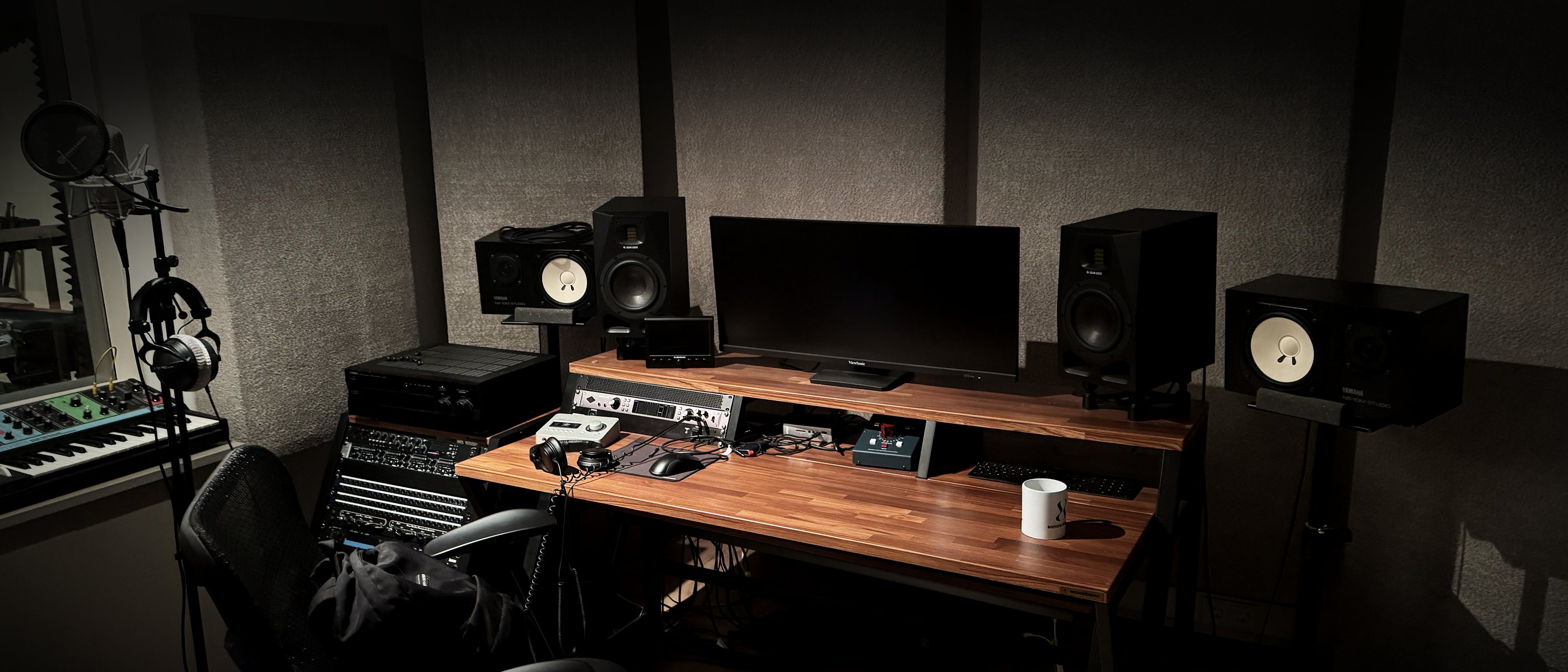 The studio in the evening: desk with monitor, speakers and acoustic panels